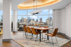A modern dining area with a large table, multiple chairs, and a city view through expansive windows. - Bach HQ | Walk to Broadway | Arcade + Pool (Nashville)