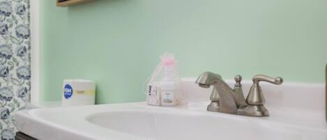 Ein Badezimmer mit einem weißen Waschbecken, einem Wasserhahn und Pflegeprodukten auf der Ablagefläche.