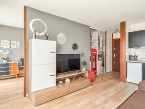 A modern living room with a TV, wooden cabinets, a red telephone booth wall art, and a kitchen area. - Apartment with terrace and garage in St-Laurent (Saint-Laurent-du-Var)