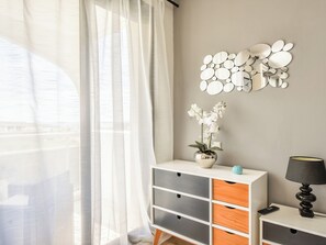 A room with a white and grey cabinet, a vase with white flowers, a wall-mounted mirror, and a lamp. - Apartment with terrace and garage in St-Laurent (Saint-Laurent-du-Var)