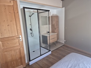 Ein Schlafzimmer mit Holzschrank, Duschkabine aus Glas, einem weißen Bett und einem Holzkasten.