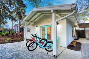 Ein überdachter Balkon mit Fahrradständer, ein kleiner Garten und ein Gebäude mit weißer Fassade und türkisblauen Akzenten.