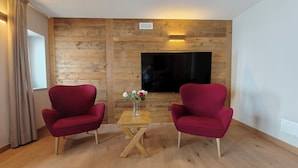 Ett rum med två röda fåtöljer, ett träbord, en vas med blommor och en platt-TV som är monterad på en väggpanel av trä.