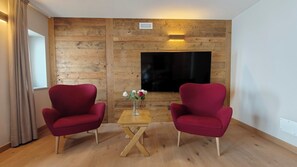 A room with two red armchairs, a wooden coffee table, a vase with flowers, and a flat-screen TV mounted on a wooden wall.
