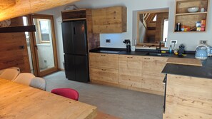 Une cuisine de taille réduite, dotée de meubles en bois, d’un réfrigérateur noir et d’un coin repas avec une table et des chaises.