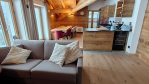 En modern inredning med ett träpanelat tak, en soffa med kuddar, en matplats med stolar och ett kök med träskåp och vitvaror.