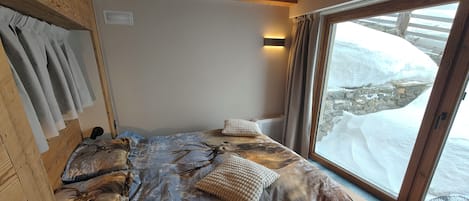 A bedroom with a large window, wooden headboard, and a bed with patterned bedding.