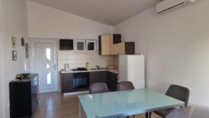 A compact kitchen with a dining area, a built-in oven, and a white refrigerator. - Apartments Ordulj (Rogoznica)