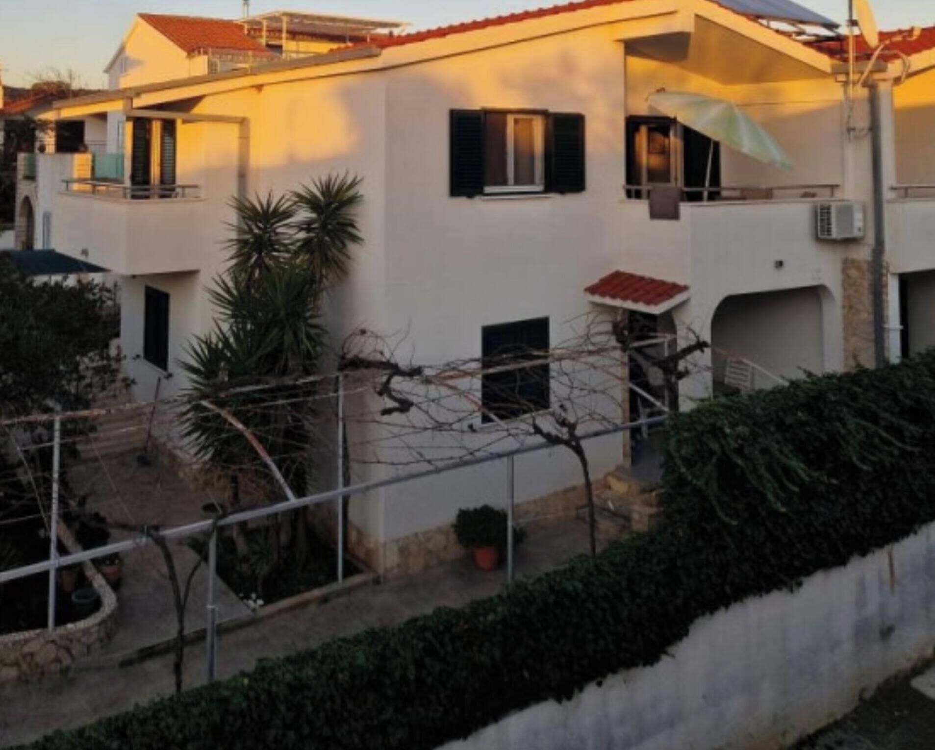 Ein zweistöckiges Gebäude mit flachem Dach, einem Balkon im oberen Geschoss und einer kleinen angebauten Garage.