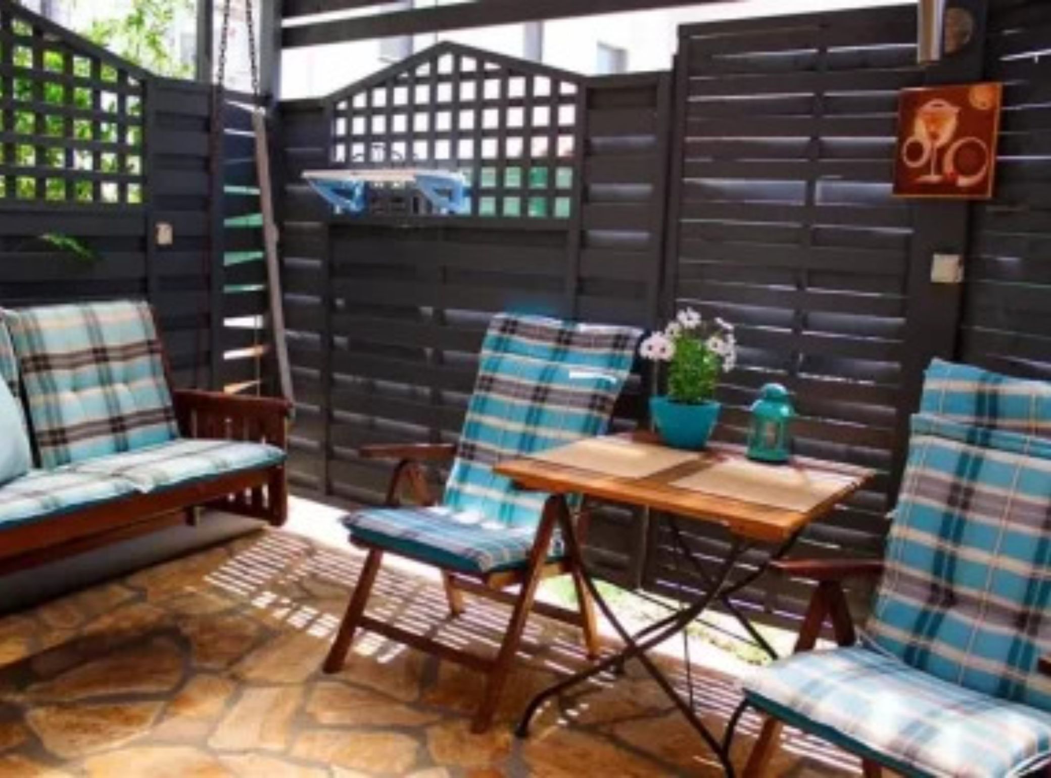 A patio with a wooden table, two chairs, a sofa, and a decorative fence.