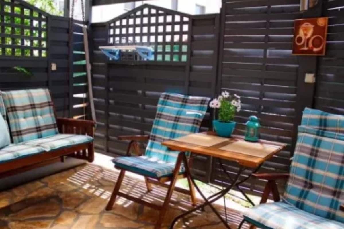 A patio with a wooden table, two chairs, a sofa, and a decorative fence.