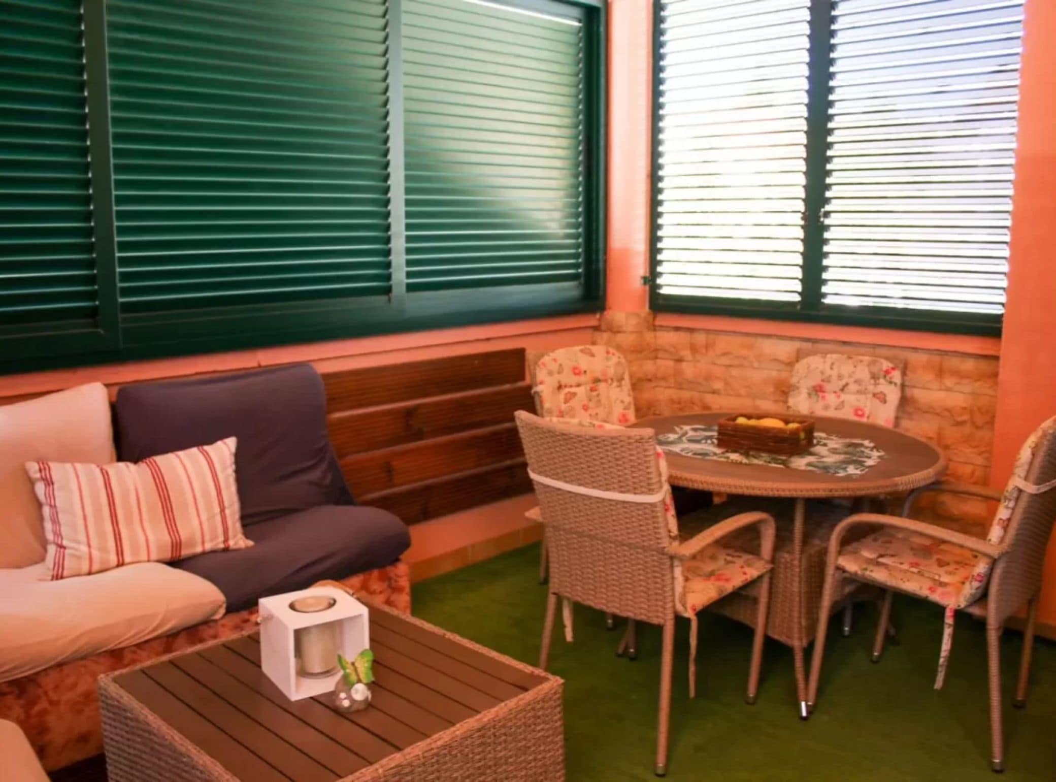 A cozy seating area with a sofa, chairs, and a table, featuring a stone wall and green blinds.
