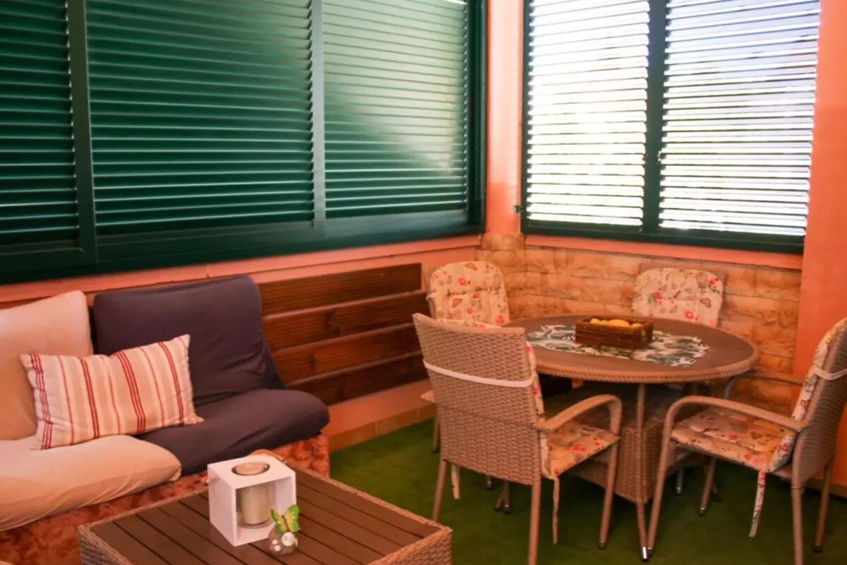Ein gemütlicher Sitzbereich mit einer Couch, Sesseln und einem Tisch, mit einer Steinwand und grünen Jalousien.