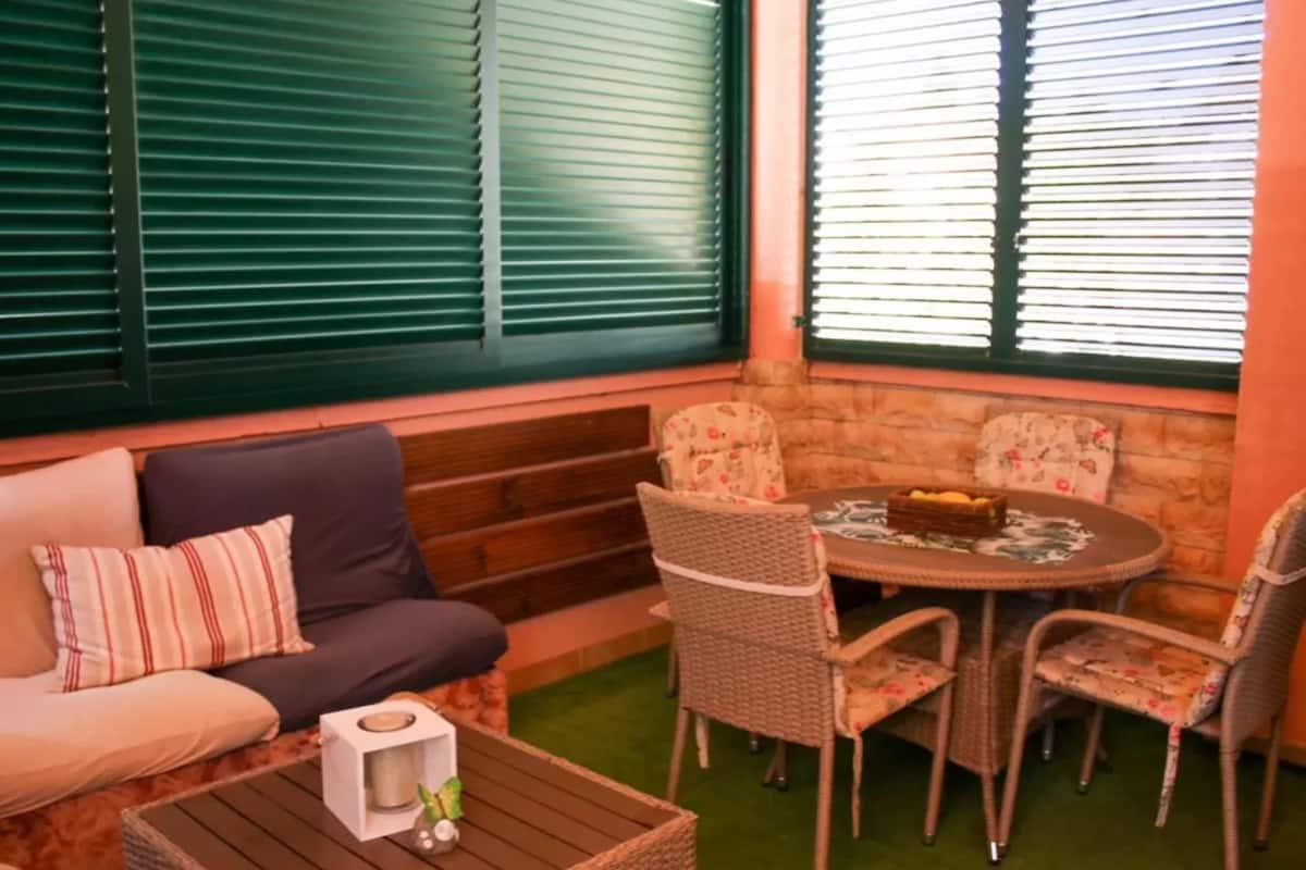 A cozy seating area with a sofa, chairs, and a table, featuring a stone wall and green blinds.