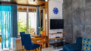 Uma sala de estar moderna com área de jantar, televisão de tela plana fixada em uma parede de pedra e uma grande janela com cortinas.
