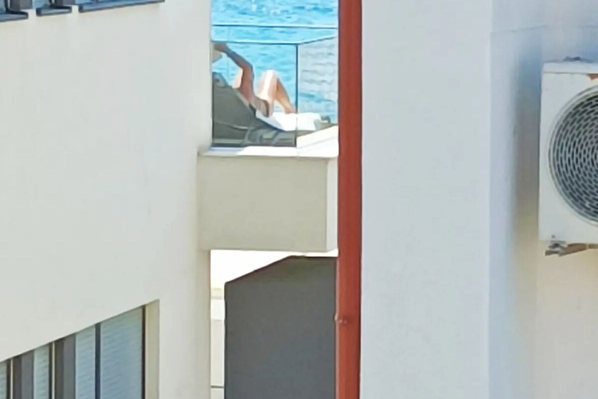 Ein Balkon mit Meerblick, eine Person entspannt und eine Klimaanlage.