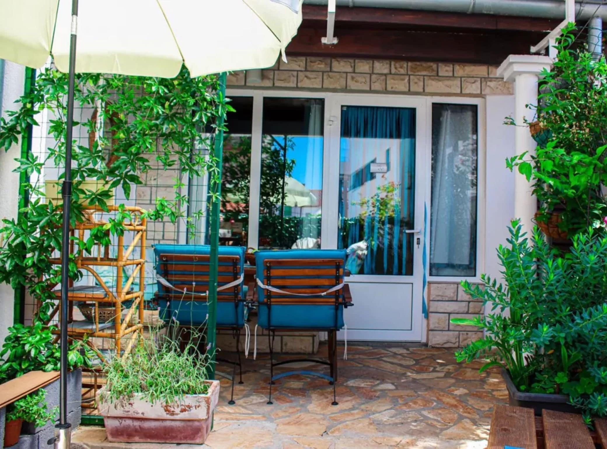 A patio with a table and chairs, a white umbrella, and potted plants.