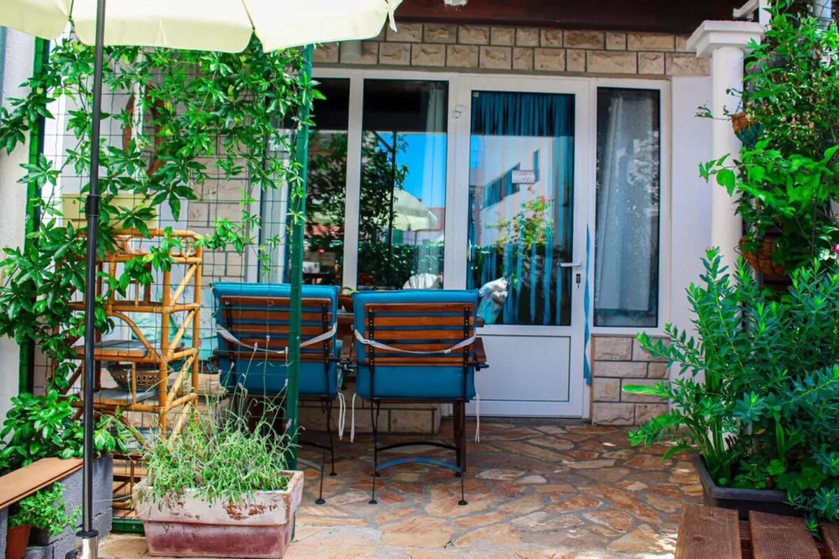 Eine Terrasse mit Tisch und Stühlen, einem weißen Sonnenschirm und Topfpflanzen.