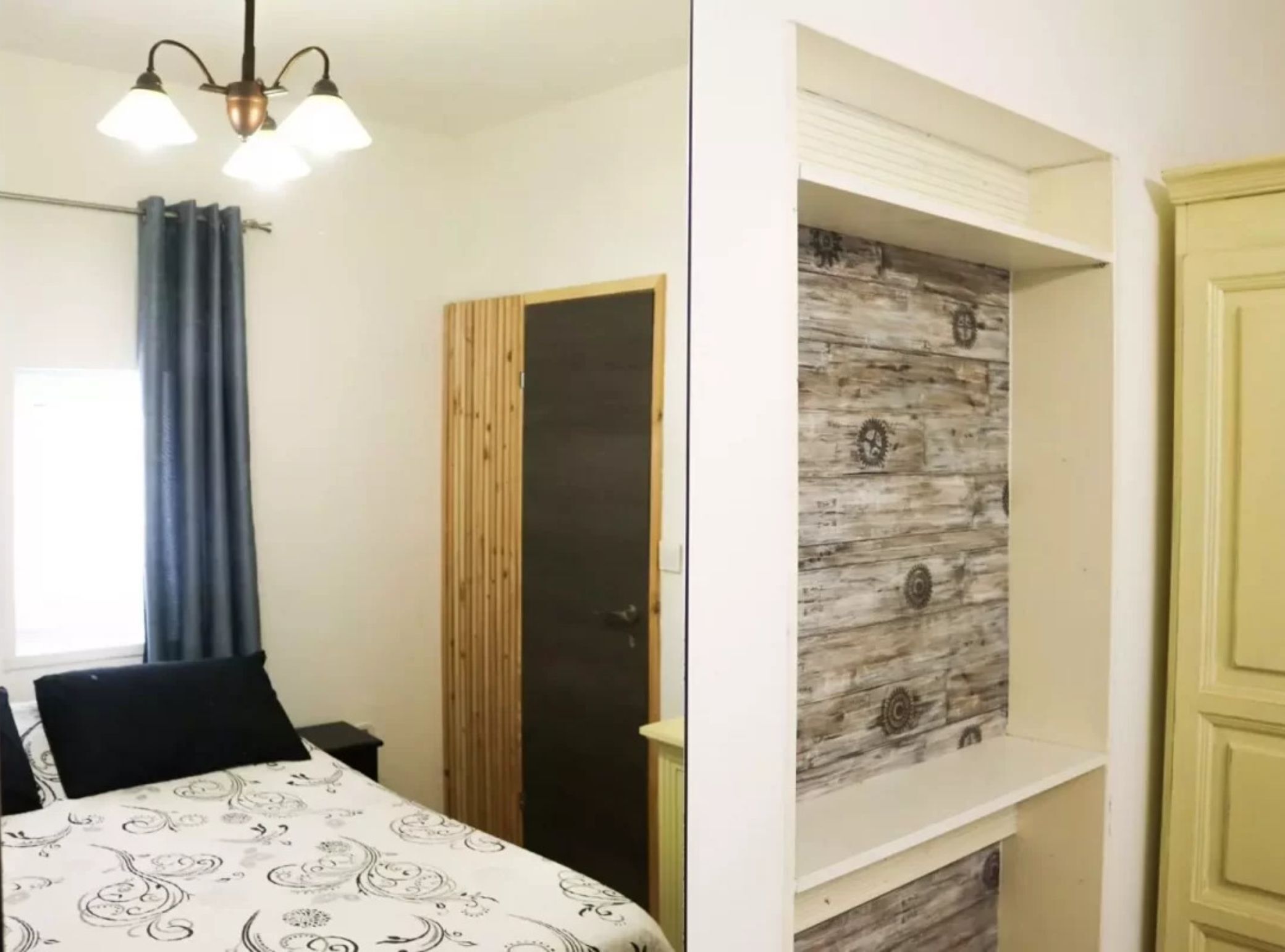 A bedroom with a bed, a wardrobe, a door, and a shelf with a rustic wall design.