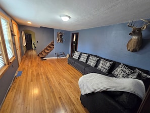 Ein Zimmer mit Holzboden, einer Couch mit gemusterten Kissen, einem aufgehängten Hirschgeweih und einer Treppe.