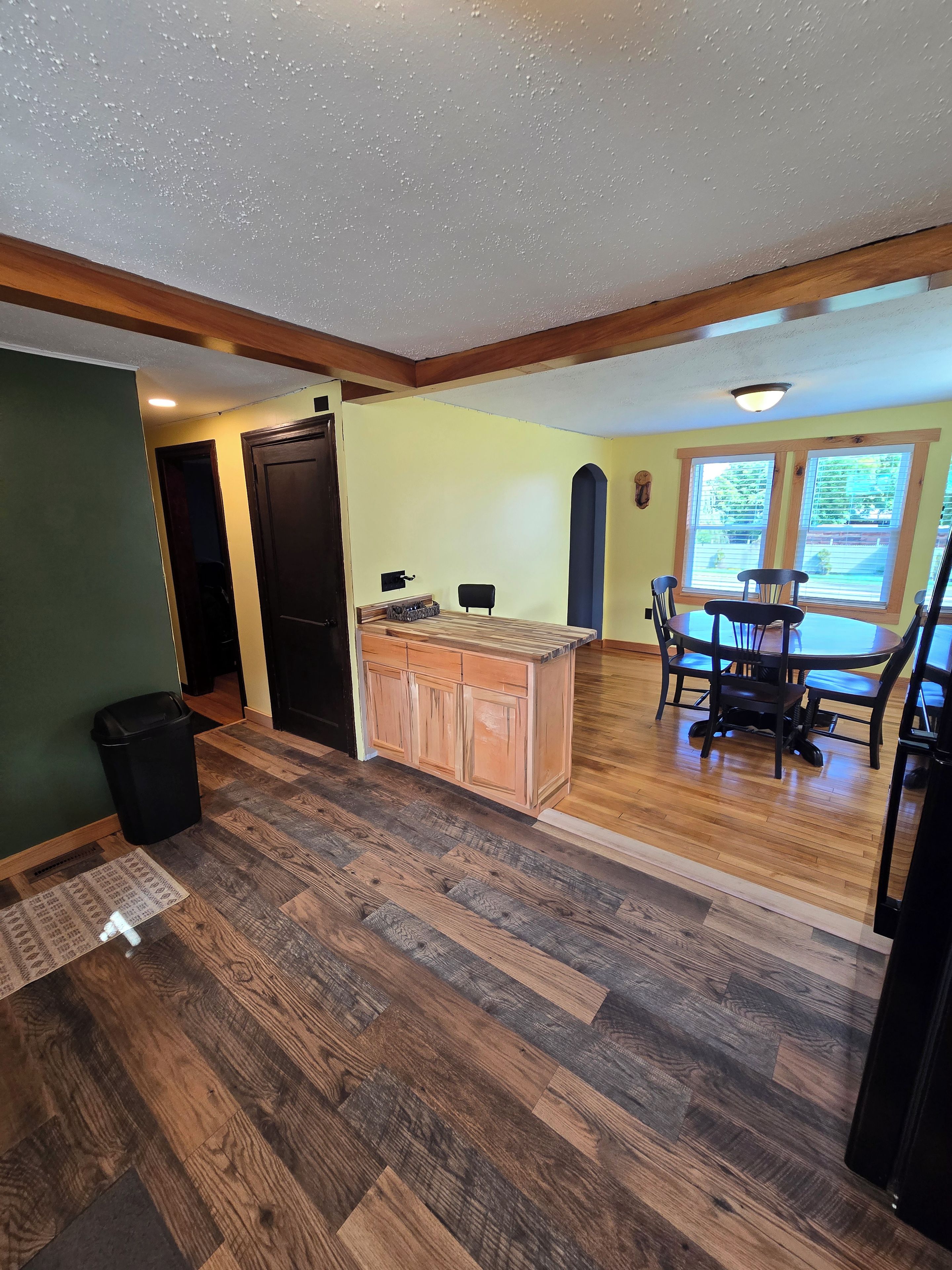 A kitchen with a wooden island, a dining area with chairs, and a window with blinds.