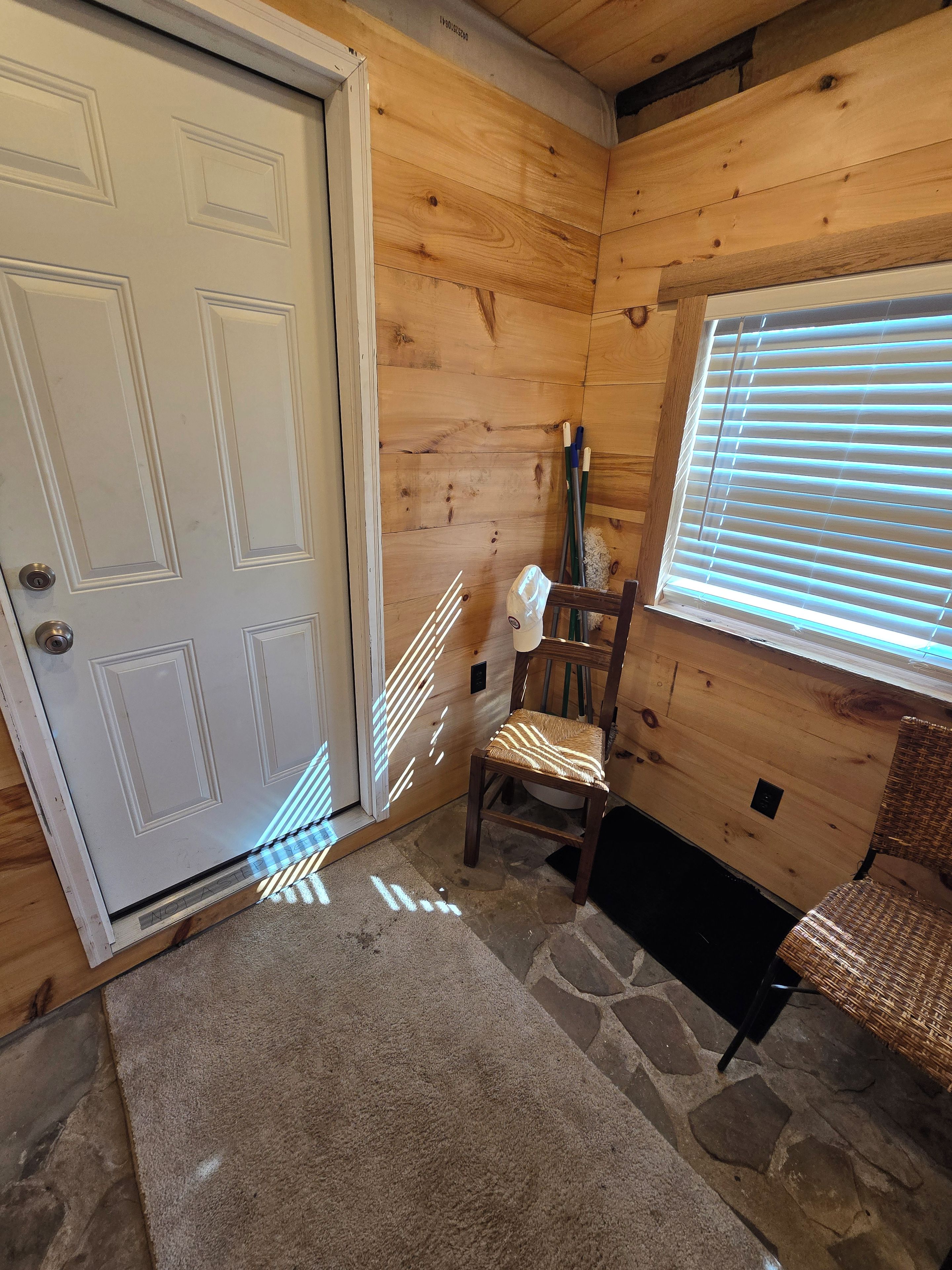 Un intérieur en bois avec une porte blanche, un sol en pierre, une chaise et une fenêtre avec des stores.