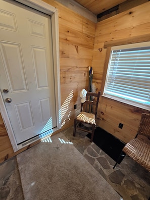 A wooden interior with a white door, a stone floor, a chair, and a window with blinds.