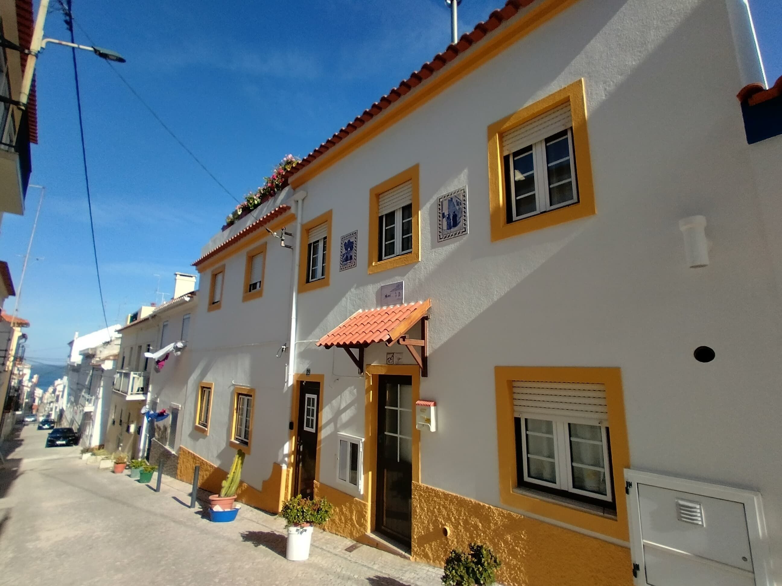 A street view of a building with a yellow and white facade, multiple windows, and a red-tiled roof.