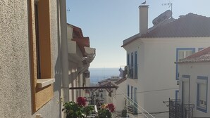 Een balkon met een geel kussen, een metalen reling en uitzicht op gebouwen en de zee.