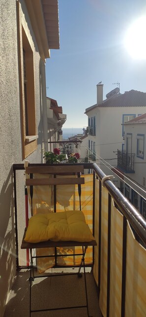 Ein Balkon mit gelber Sitzauflage, Metallgeländer und Blick auf Gebäude sowie das Meer.