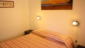 Een slaapkamer met een bed, twee wandlampen, een schilderij en een lijst met een foto aan de muur.
