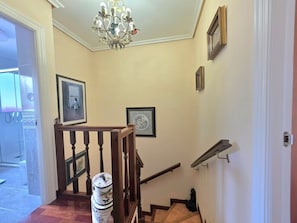 Un escalier avec des rampes en bois, un lustre et des tableaux encadrés accrochés aux murs.