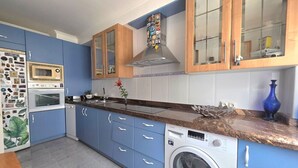 A compact kitchen with blue cabinets, a built-in oven, a microwave, a stainless steel range hood, and a washing machine. - Apartment Ora al Mare - 32002 (Pedreña)