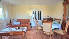 Una sala de estar con sofá, sillas, una mesa de comedor y una puerta que da a otra habitación.