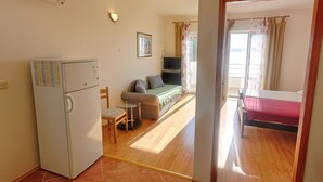 Et lille værelse med køleskab, et lille bord, en sofa, en seng og et fjernsyn.