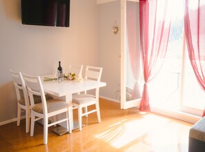 A dining area with a white table, four chairs, a bottle, glasses, and a small flower arrangement. - Comfort Villa Šolo (Ploce)