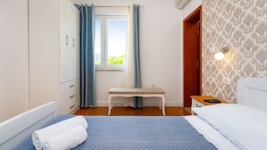 Ein Schlafzimmer mit einem Bett, einer Sitzbank, einem Kleiderschrank, einem Fenster mit Vorhängen und einer Wandleuchte.