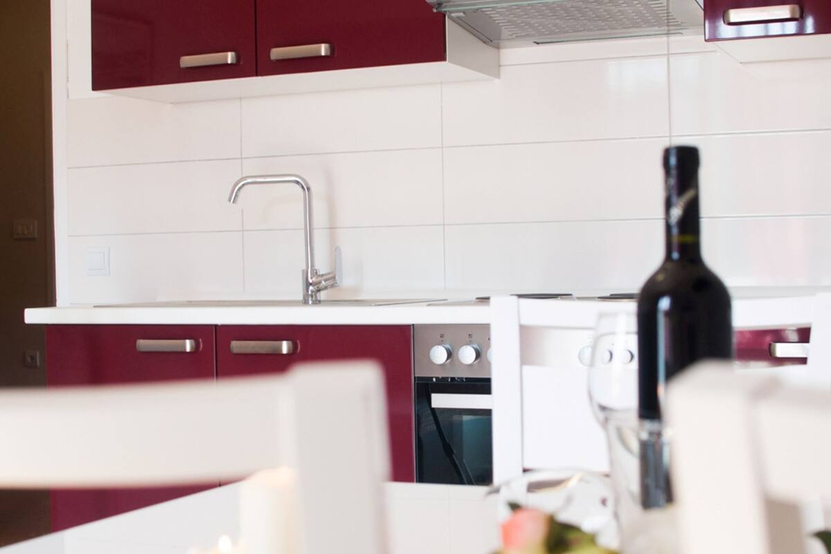 A modern kitchen with white cabinets, a stainless steel faucet, and a wine bottle.