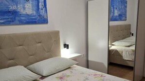 Une chambre à coucher avec un lit, une table de chevet, un miroir et un tableau bleu accroché au mur.