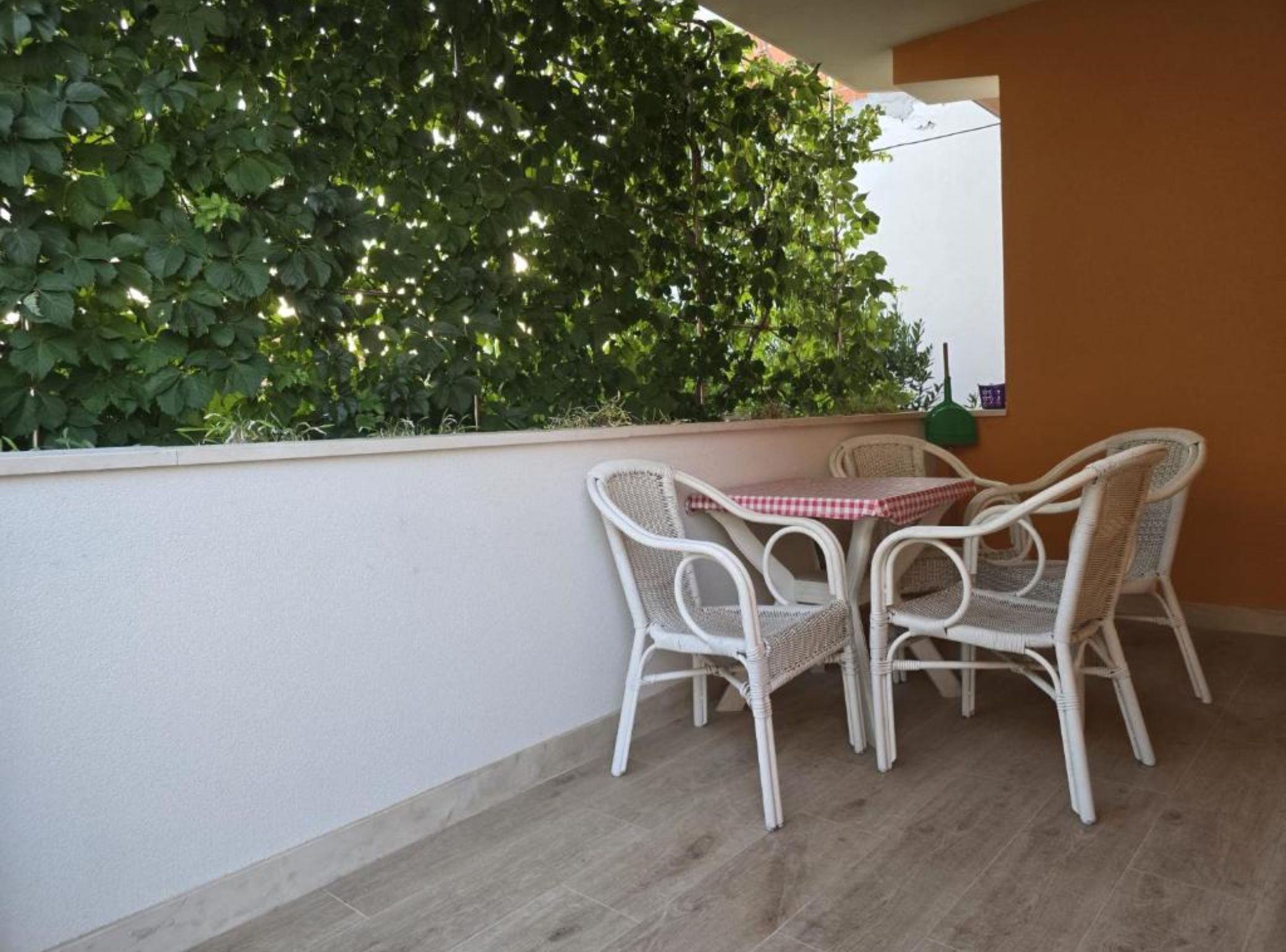 A balcony with a white wicker table and chairs, a checkered tablecloth, and a green hanging plant.