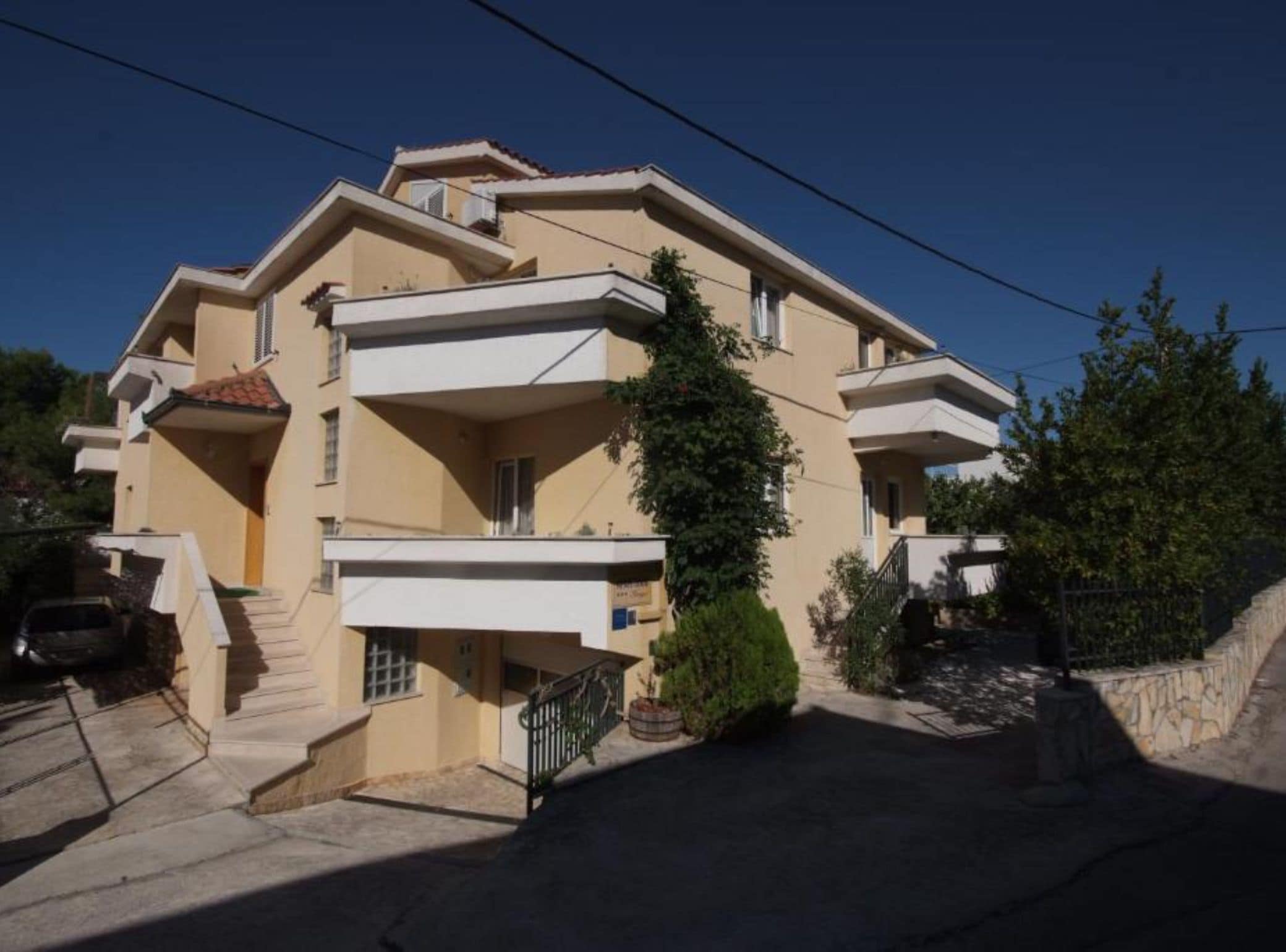 A multi-story residential building with balconies, a staircase, and a paved driveway.