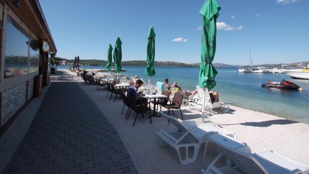 Un restaurant en bord de mer avec une terrasse, des parasols verts et une vue sur la mer et les bateaux.