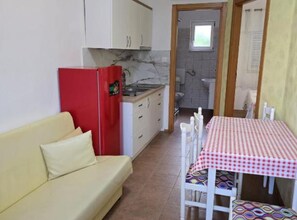 A compact kitchenette with a red refrigerator, a small dining table with a checkered tablecloth, and a beige sofa. - Apartments Gogi (Okrug)