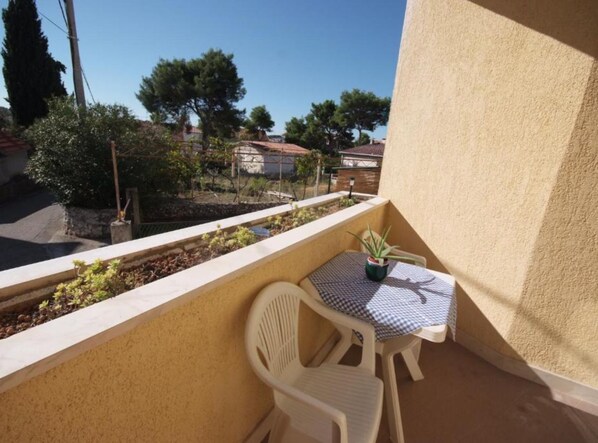 A balcony with a small table and chairs, a potted plant, and a view of houses and trees. - Apartments Gogi (Okrug)