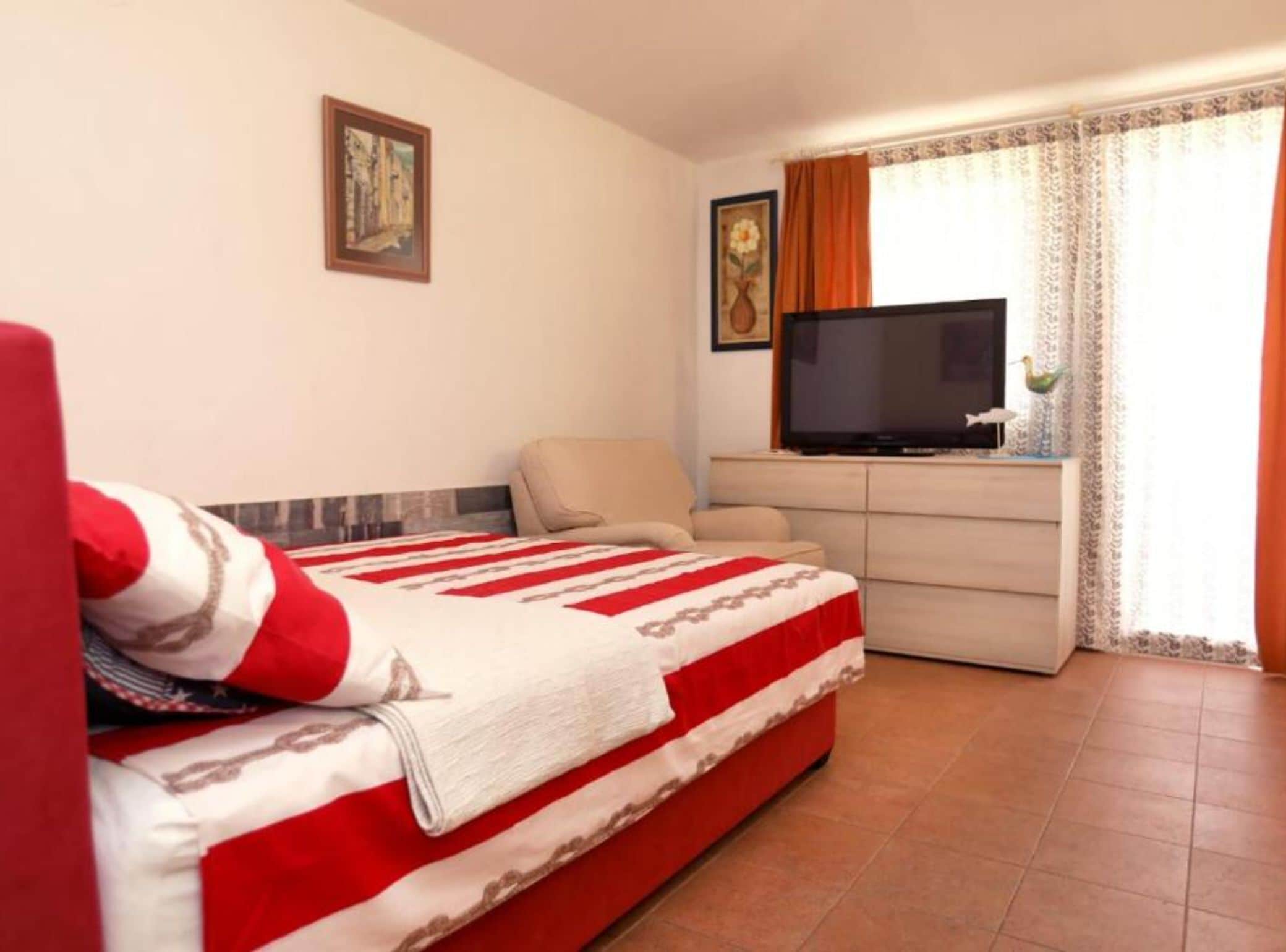 A hotel room with a bed, a television, a desk, and a window with curtains.