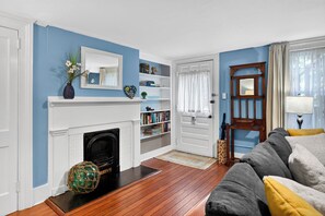 A living room with a fireplace, bookshelves, a sofa, and a door leading to another room. - Charming One-Bedroom Apartment on Beautiful Taylor Square (Savannah)