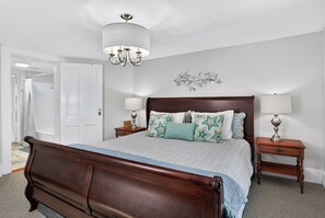 A bedroom with a wooden bed, two bedside tables, a chandelier, a door, and a wall decoration. - Charming One-Bedroom Apartment on Beautiful Taylor Square (Savannah)
