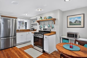 A modern kitchen with stainless steel appliances, white cabinetry, and a wooden dining table. - Charming One-Bedroom Apartment on Beautiful Taylor Square (Savannah)