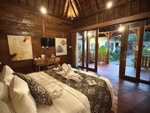 A wooden interior with a bed, artwork, a desk, and a view of an outdoor area.