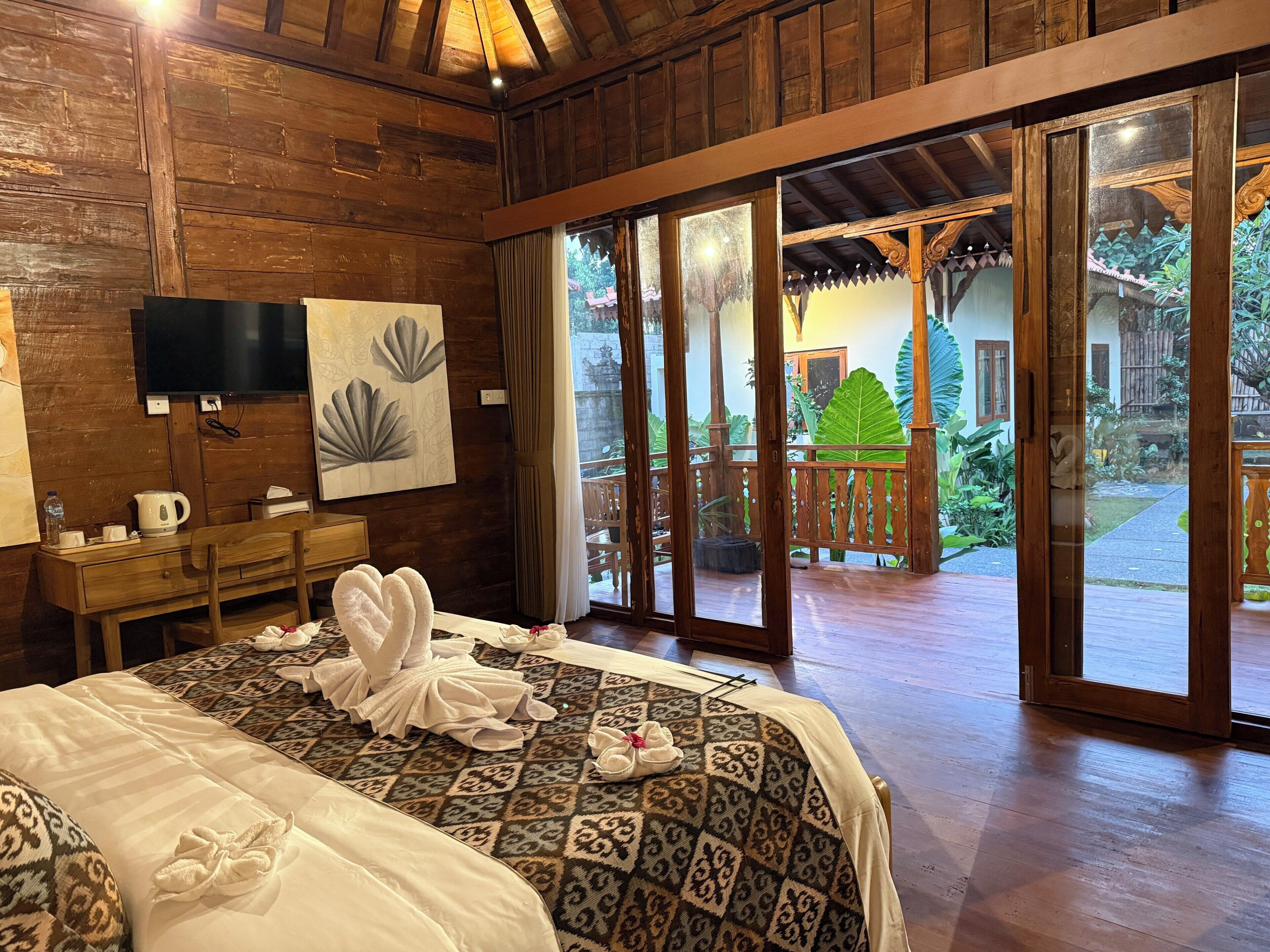 A hotel room with a bed, a desk, a television, and a view of the outdoor area.